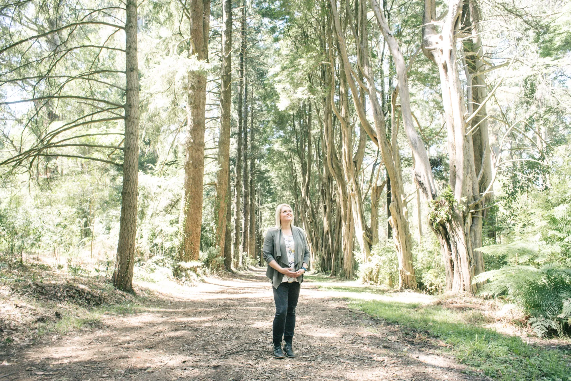 Margaret Moore standing in a sunlit forest, looking up through the trees